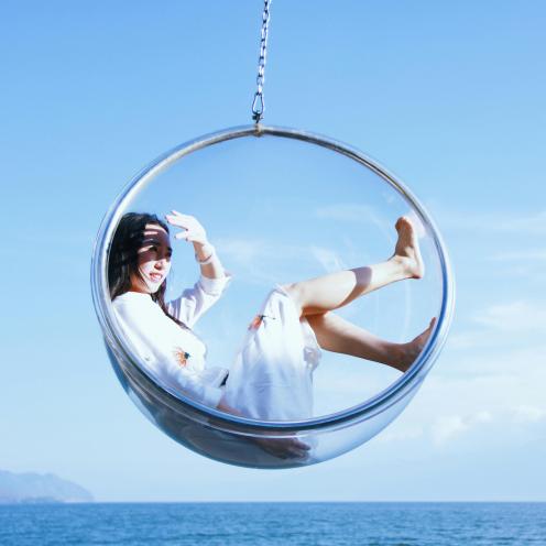 Een vrouw zit in een halve glazen bol die boven de oceaan lijkt te zweven.